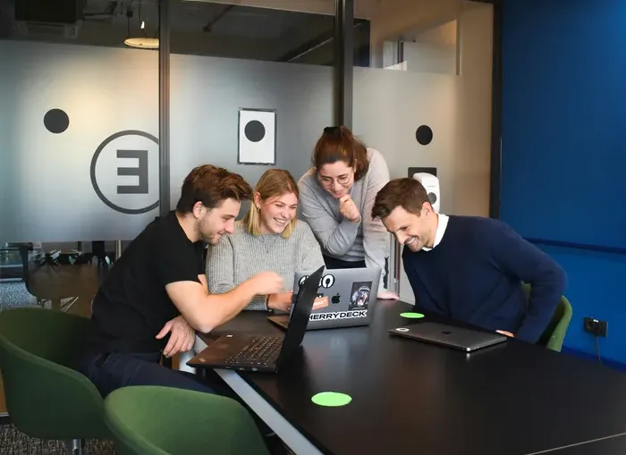 Team of colleagues around a laptop in a bright office, smiling and planning next steps together during a meeting